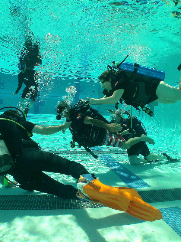 Adaptive scuba diver swimming confidently with buddy divers in pool
